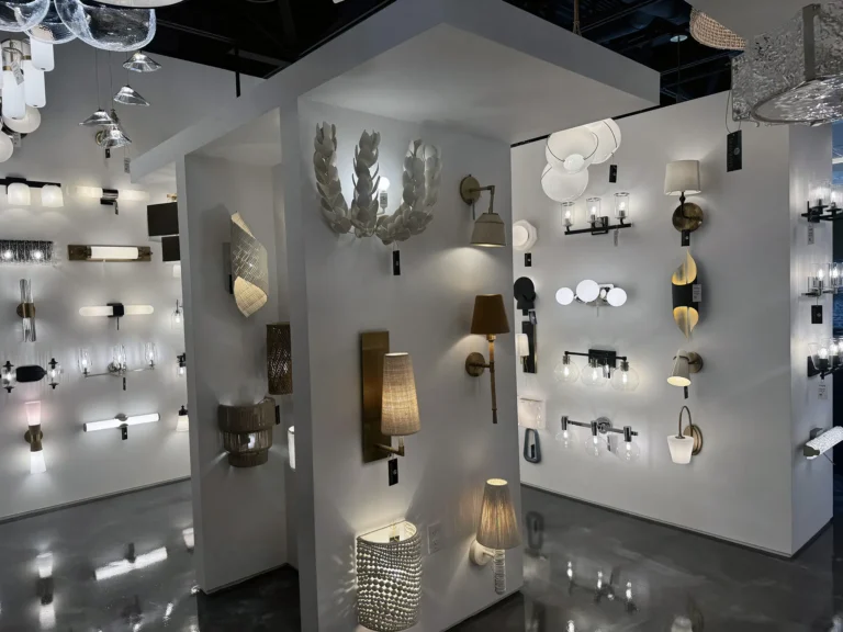Showroom displaying a variety of modern wall light fixtures mounted on white walls, with different shapes, colors, and materials, all illuminated in a well-lit, glossy-floored interior.