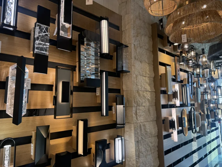 A display wall featuring various modern and decorative wall lights, including glass, metal, and wood designs, arranged in rows with a mix of rectangular and cylindrical shapes in a showroom setting.